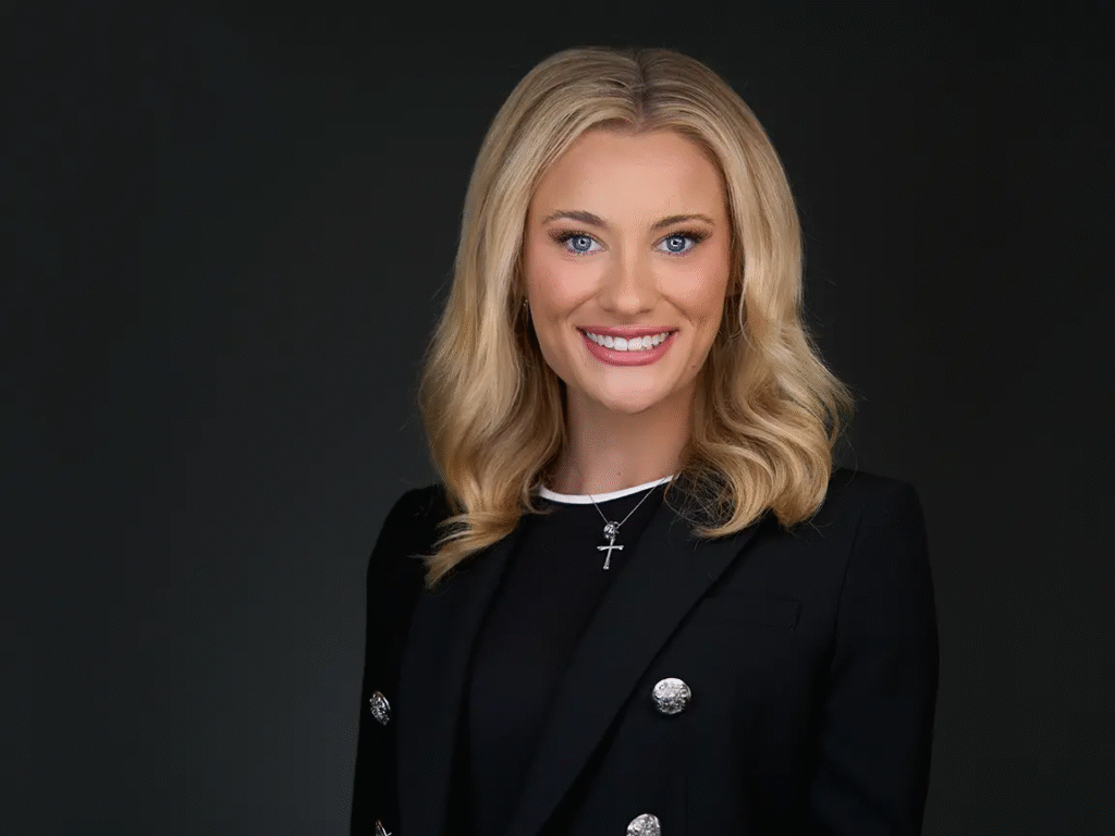 Professional headshot of a woman with blonde hair wearing a black blazer and cross necklace.