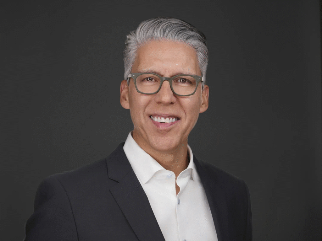 Professional headshot of a man in glasses and a dark suit with a white shirt.