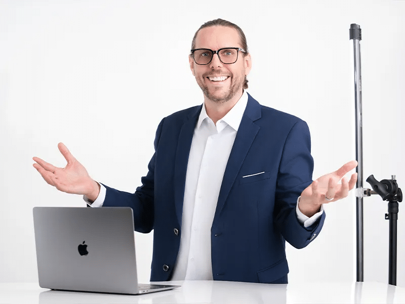 Best Ways To Prepare For A Successful Portrait Shoot 30 Smiling man in a suit behind a laptop, arms open, white background.