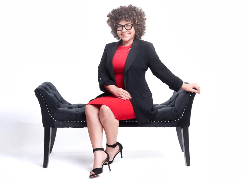 Best Ways To Prepare For A Successful Portrait Shoot 29 Woman in red dress and black blazer sitting on a bench, white background.