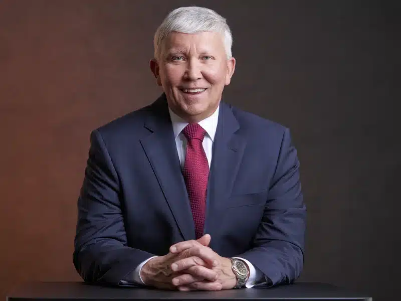 Top 10 Ways Business Headshots Improve Your Personal Brand 28 Smiling person in a navy suit and red tie, seated with hands clasped on a table.