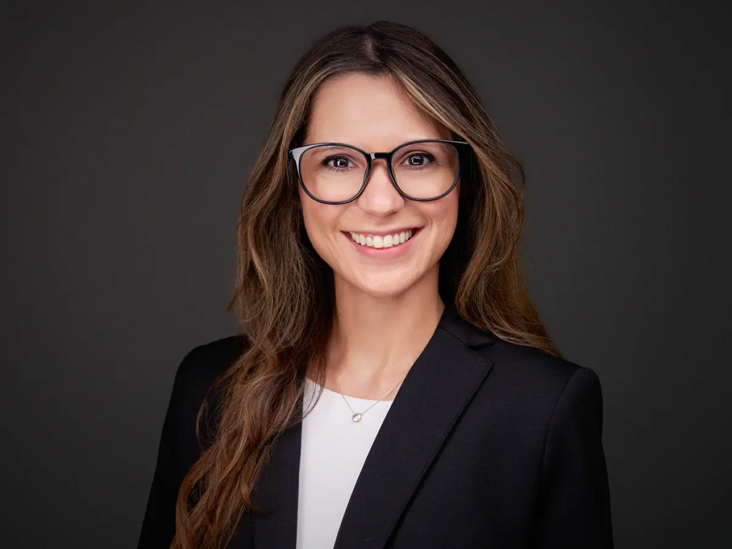 Top 10 Ways Business Headshots Improve Your Personal Brand 31 Smiling person wearing glasses and a black blazer against a dark background.