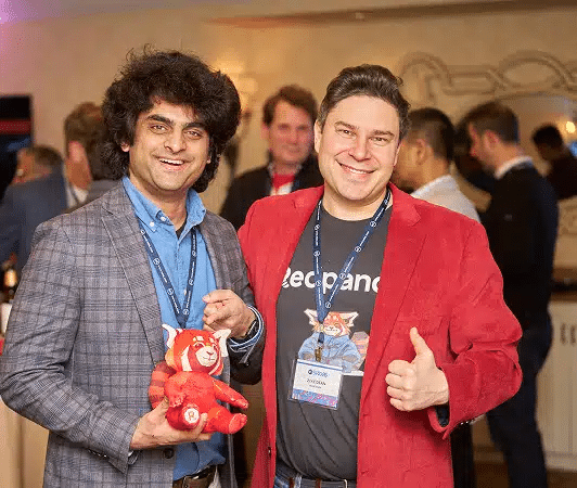 How Conference Photography Supports Your Marketing Team 30 Two men at a conference smile for the camera, one holding a red stuffed animal while the other gives a thumbs-up.