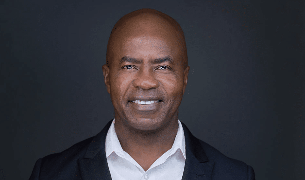 A man in attorney attire—dark suit and white shirt—smiles at the camera against a plain dark background, perfect for lawyer professional photos.