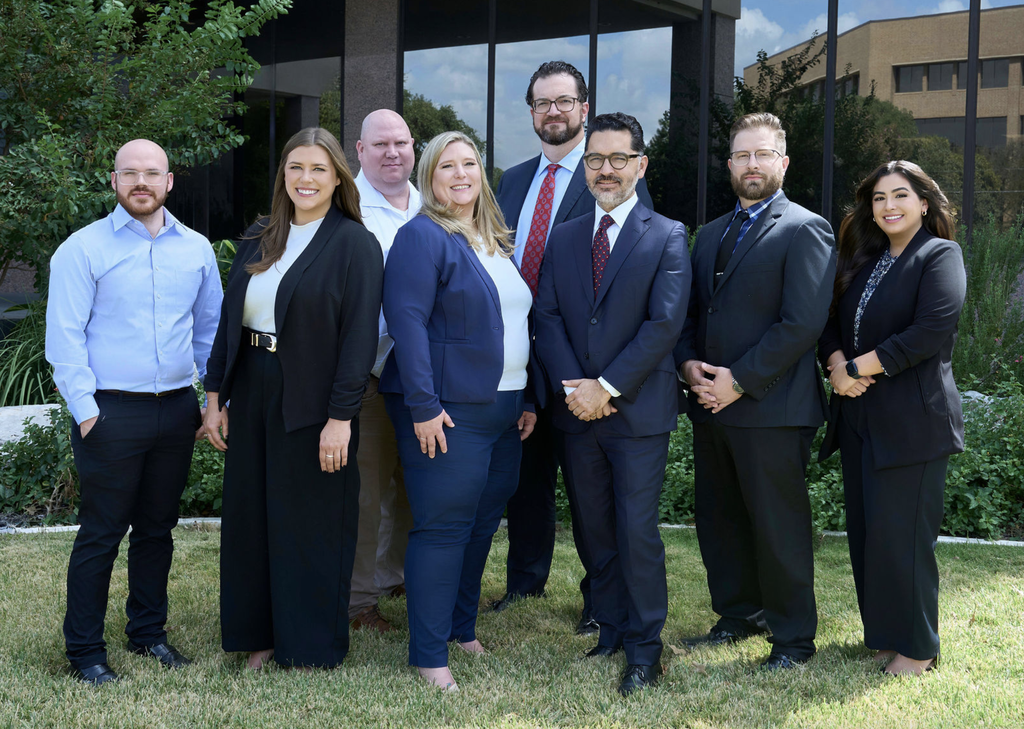 Professional corporate team portrait of seven business professionals standing outside an office building.